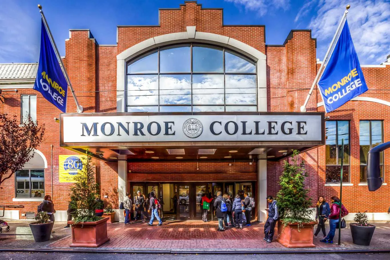 Entrance to a red-brick campus building with a large arched window above a marquee reading 'MONROE COLLEGE'